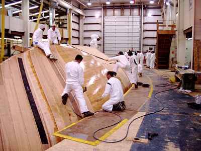 Workers dressed in Tyvek coveralls laying-up the timber plies on a Hodgdin hull.  The state-of-the-art, cold-moulded, wood-epoxy technique produces the ultimate custom hull.